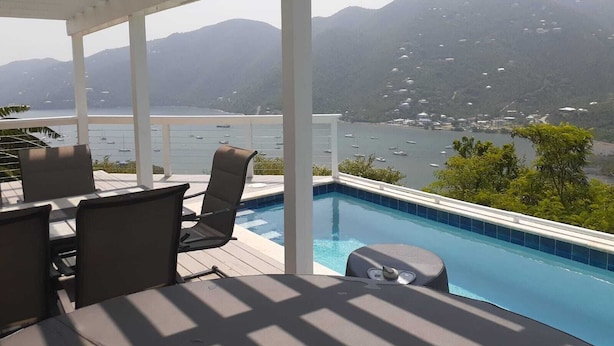 Un espace aménagé au bord de la piscine, offrant une vue sur une baie et des montagnes.