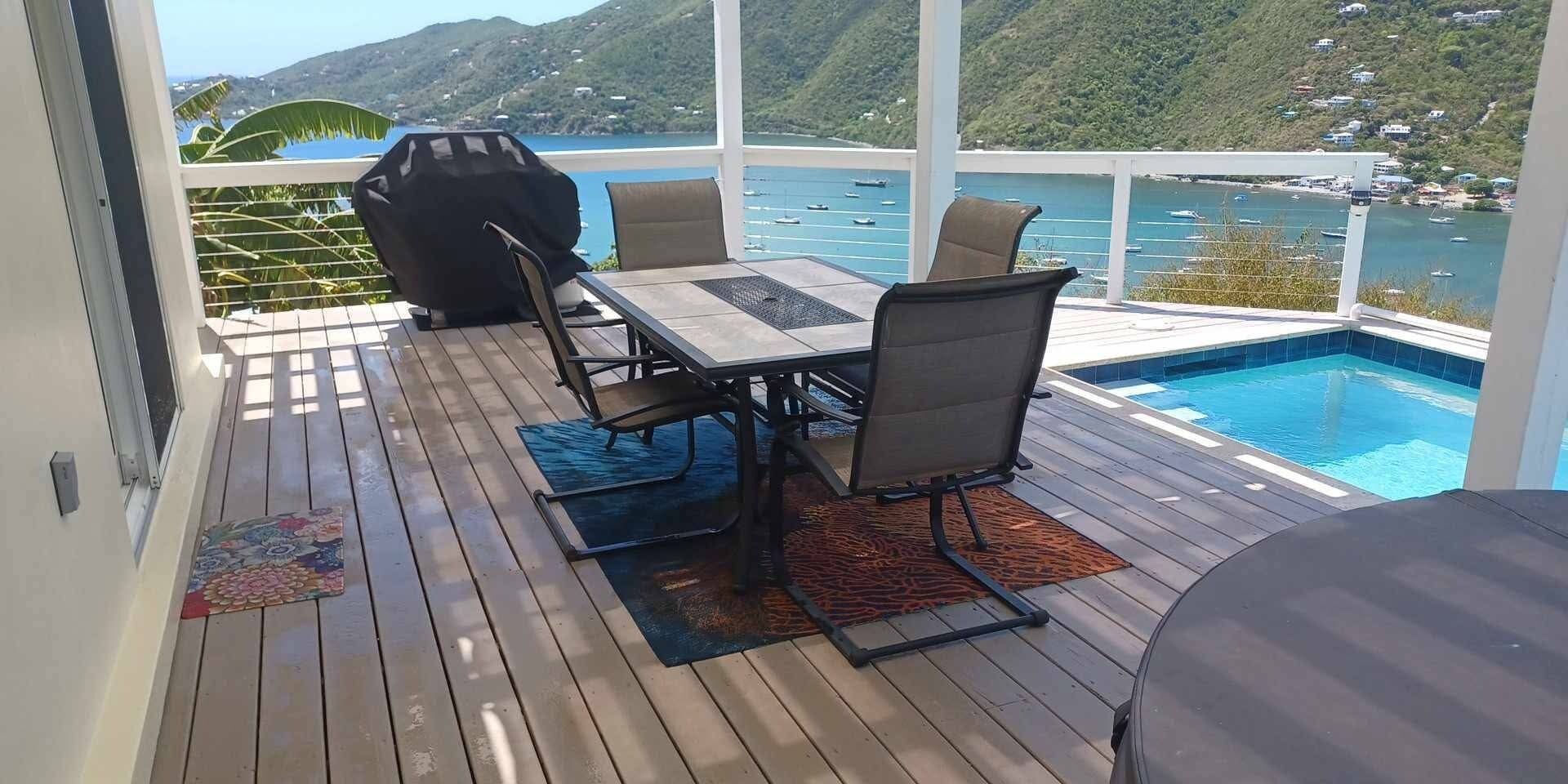 Eine Terrisse im Freien mit Pool, Tisch, Stühlen und Grill.