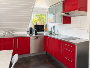 A modern kitchen with red cabinets, a dishwasher, a coffee maker, and a window overlooking greenery.