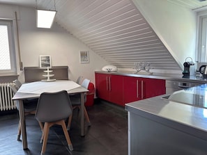 A modern kitchen with a dining area, red cabinets, and a white ceiling.