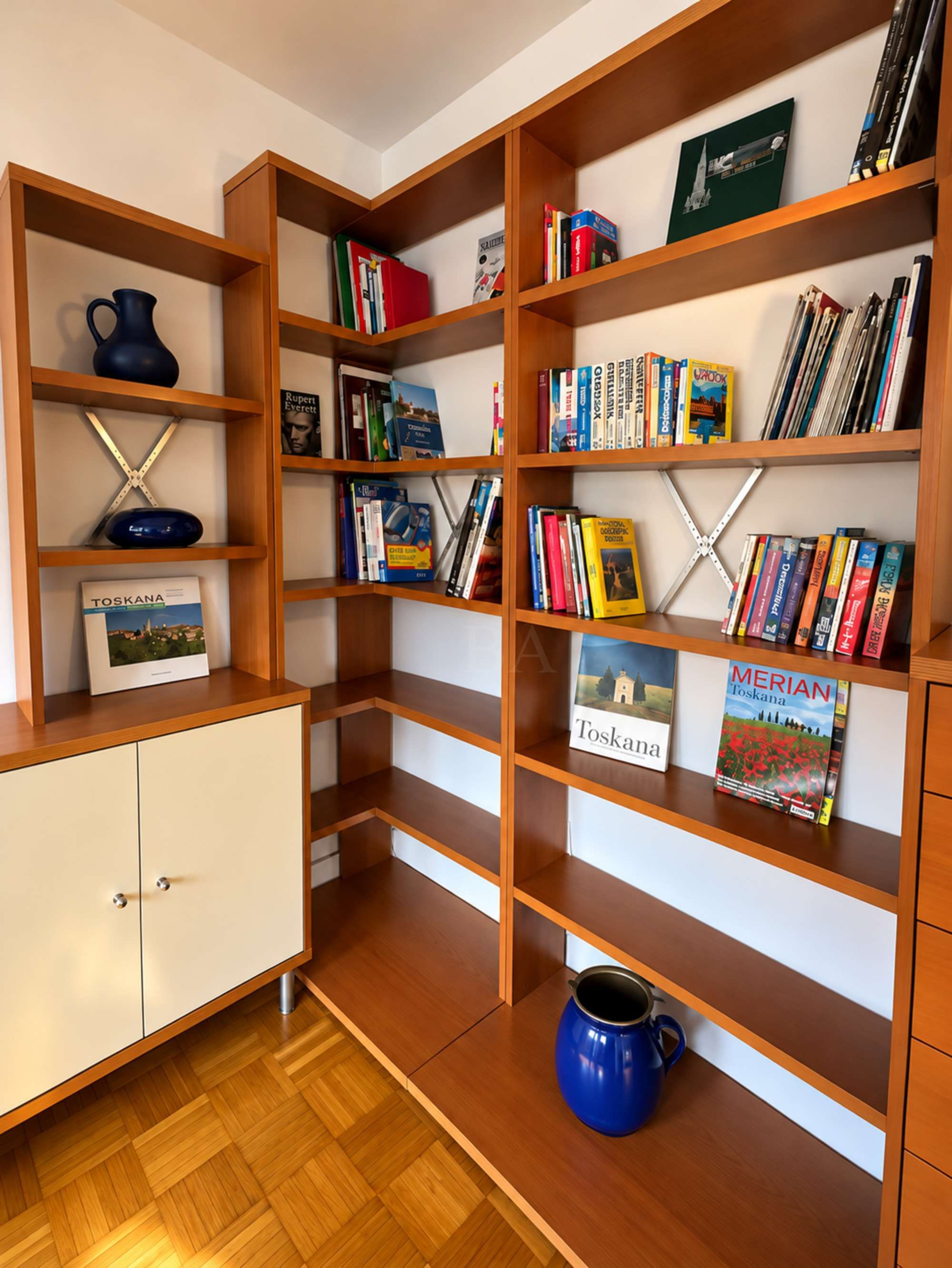 A room with wooden bookshelves filled with books and a white cabinet with a blue vase.