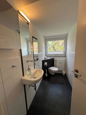 A modern bathroom with a white sink, black toilet, and a window with a view of trees.