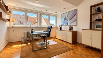 Ein moderner Büroraum mit Schreibtisch, Stuhl, Heizkörper, Fenstern und Bücherregal.