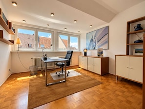 A modern office space with a desk, chair, radiator, windows, and a bookshelf.