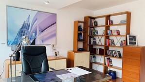 A modern office with a desk, chair, bookshelf, and a large window with a cityscape view.