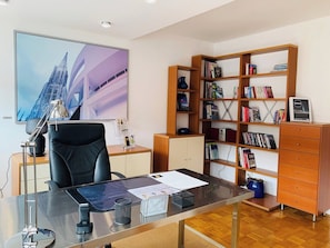 A modern office with a desk, chair, bookshelf, and a large window with a cityscape view.