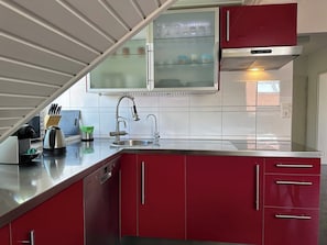 A modern kitchen with red cabinets, a stainless steel sink, and a built-in oven.