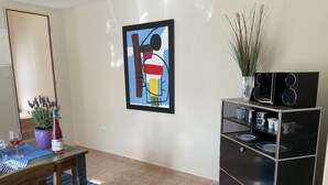 A modern living room with a dining area, a black entertainment unit, a framed abstract painting, and a potted plant. - Paradis de Provence (Le Pin)