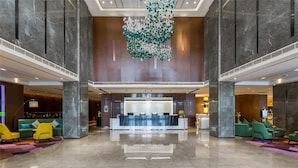 Een ruime lobby met een receptiebalie, zithoeken en een decoratieve installatie aan het plafond.