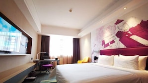 Een hotelkamer met een groot bed, een bureau met stoel, een televisie en een raam met gordijnen.