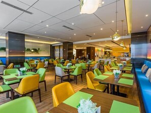 A modern dining area with green and yellow chairs, wooden tables, and a blue sofa. - Hampton BY Hilton Shiyan Yunyang (Shiyan)