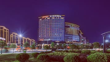 Un hotel moderno con fachada curva, señalización iluminada y zonas verdes bien cuidadas con árboles y farolas.