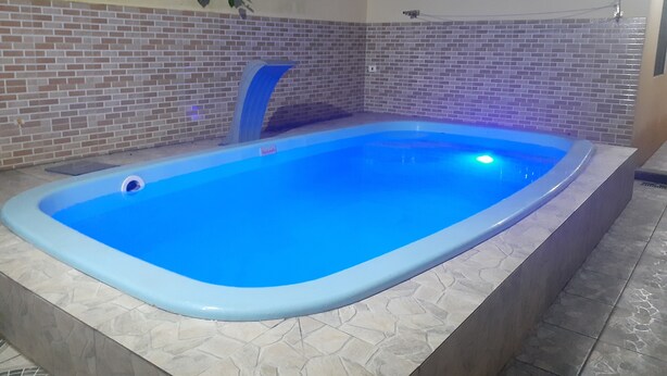 Una piscina rectangular con revestimiento azul, rodeada por un muro de baldosas con diseño de ladrillo.