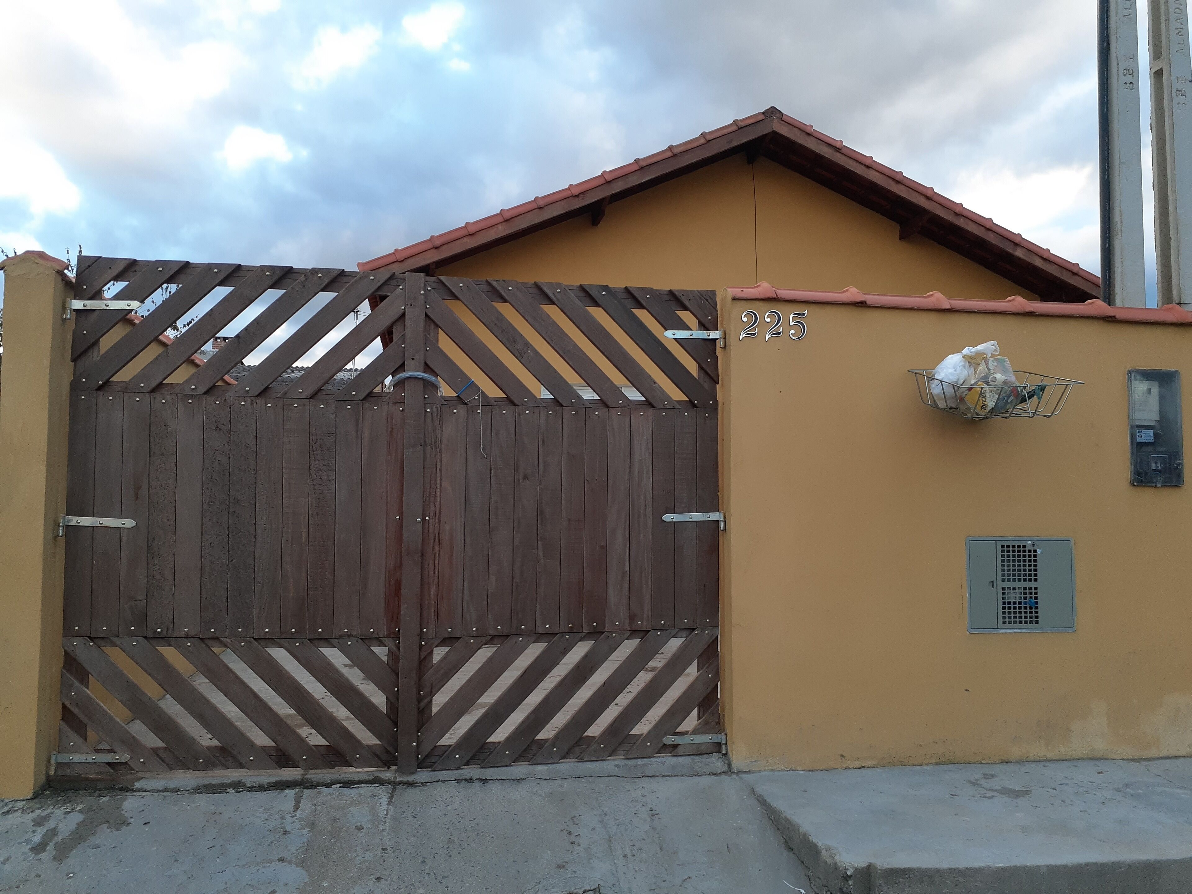 A gated entrance with a number 225 sign, a metal basket on the wall, and a vent.