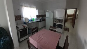 Una cocina compacta con armarios blancos, un refrigerador, una estufa y una mesa de comedor con sillas.