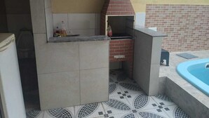 Cocina exterior con horno de ladrillo, piso de baldosas y zona de piscina.