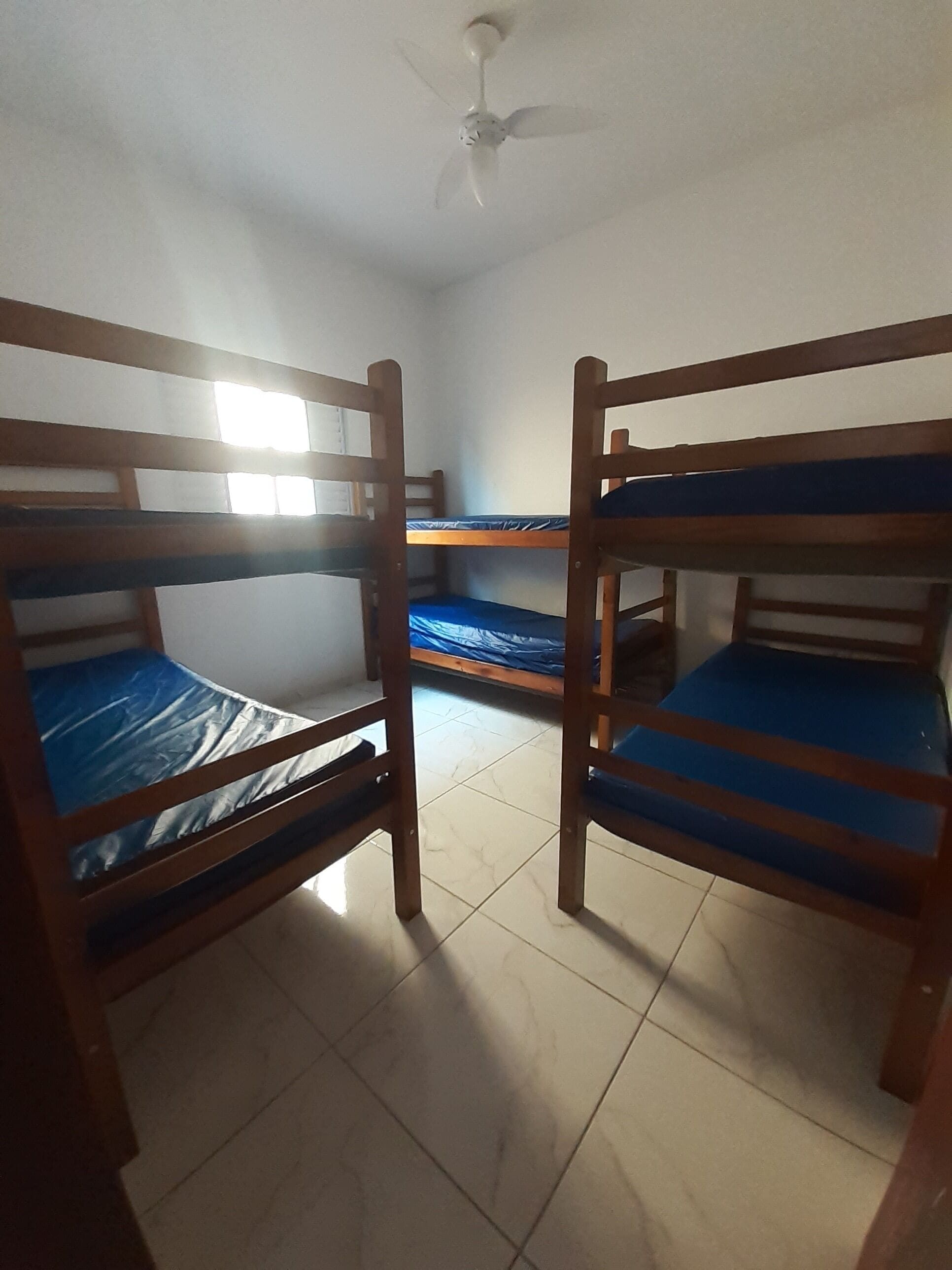 Une chambre avec deux lits superposés, un ventilateur de plafond et une fenêtre laissant entrer la lumière naturelle.