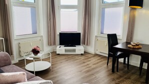 Un salon moderne avec un téléviseur à écran plat, une table à manger avec des chaises et une table basse ronde.