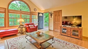 A spacious living room with a large arched window, a red leather sofa, a wooden coffee table, and a television on a wooden cabinet.
