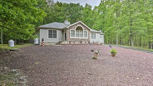 A house with a stone facade, a driveway, and a gravel area with a windmill and a potted plant.