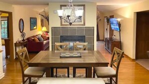 A dining area with a wooden table and chairs, a chandelier, and a fireplace.