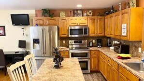 A kitchen with wooden cabinets, stainless steel appliances, a granite countertop, and a dining area with a chair.