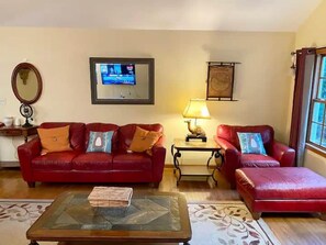 A living room with a red sofa, a coffee table, a TV, a lamp, and a window.