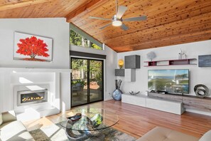 A modern living room with a fireplace, a large flat-screen TV, and a ceiling fan. - Sunset Villa: Upscale Three Bedroom Three Bath with Ocean Views (Pebble Beach)