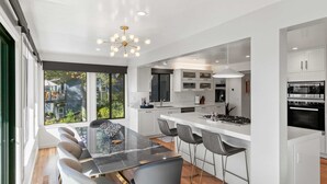 Una cocina moderna con armarios blancos, una isla central con taburetes y un amplio ventanal con vistas al exterior.