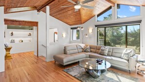 Una sala de estar moderna con techo de madera, ventanas amplias, un sofá modular y una mesa de centro de vidrio.