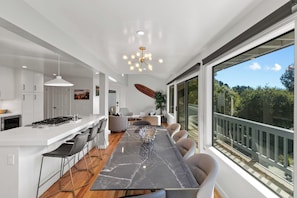 Una cocina moderna con encimera de mármol, un comedor con una mesa grande y vistas al exterior a través de amplios ventanales.