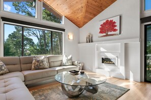 A modern living room with a glass coffee table, beige sofa, and a fireplace. - Sunset Villa: Upscale Three Bedroom Three Bath with Ocean Views (Pebble Beach)