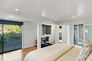 Ein modernes Schlafzimmer mit einem großen Bett, einem Schreibtisch und Blick auf den Garten.