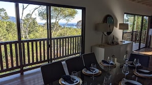 A dining area with a table set for four, large windows with a view of trees and hills, and a balcony with a railing. - Pacific Panorama: Stunning Ocean Views and Pacific Sunsets (Carmel)