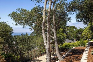 A landscaped garden with mature trees, a stone pathway, and a view of the sea.