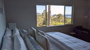 A bedroom with a large window, a bed, a chair, and a small table.