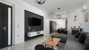 A modern living room with a sofa, a wooden coffee table, and a TV mounted on a black wall. - Elysian Villa in Afantou (Αφάντου)