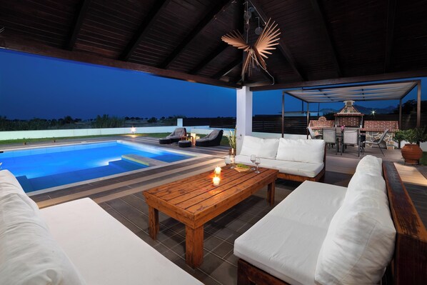A covered outdoor area with a pool, seating, and a barbecue.