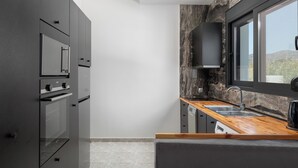 A modern kitchen with dark cabinetry, a wooden countertop, and a large window. - Elysian Villa in Afantou (Αφάντου)