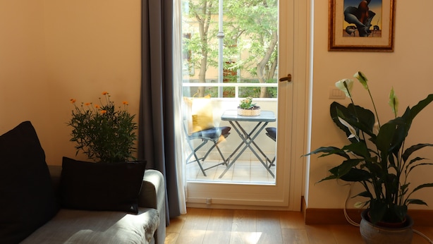 Une pièce comprenant un canapé, une petite table, une plante en pot et une vue sur un espace extérieur aménagé avec une table et des chaises, accessible par une porte vitrée.