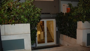 Une entrée d’immeuble avec une porte en verre, un escalier et de la verdure environnante.