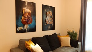 Un salon avec un canapé gris, des coussins noirs et jaunes, et deux tableaux abstraits accrochés au mur.