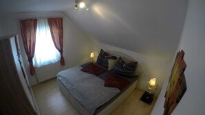 A bedroom with a bed, two bedside lamps, a window with curtains, and a radiator.