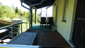 A covered outdoor area with a wooden deck, metal railing, and a table with chairs. - Vacation apartment Burgblick 2 (Großlohra)