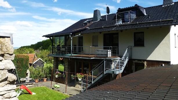 A two-story house with a balcony, a stone wall, and a garden area. - Vacation apartment Burgblick 2 (Großlohra)
