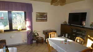 A dining area with a table set for two, a television, and a window with curtains. - Vacation apartment Burgblick 2 (Großlohra)