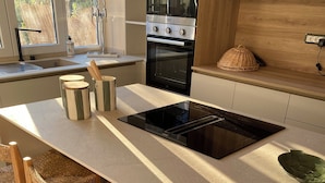 A modern kitchen with a central island, built-in oven, and a dining area with wicker chairs. - Casa Riservata Immersa Nella Natura con Spiaggia Raggiungibile a Piedi (Toscana)