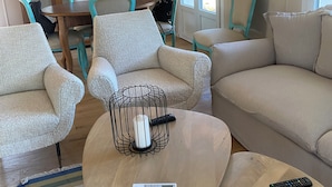 A living room with a sofa, armchairs, a coffee table, a chandelier, a dining table with chairs, and a view through a window. - Casa Riservata Immersa Nella Natura con Spiaggia Raggiungibile a Piedi (Toscana)