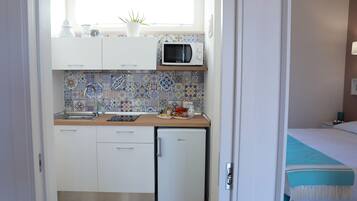 Una cocina compacta con microondas, fregadero y un refrigerador pequeño. Hay una ventana sobre el fregadero y una planta en maceta en la encimera.