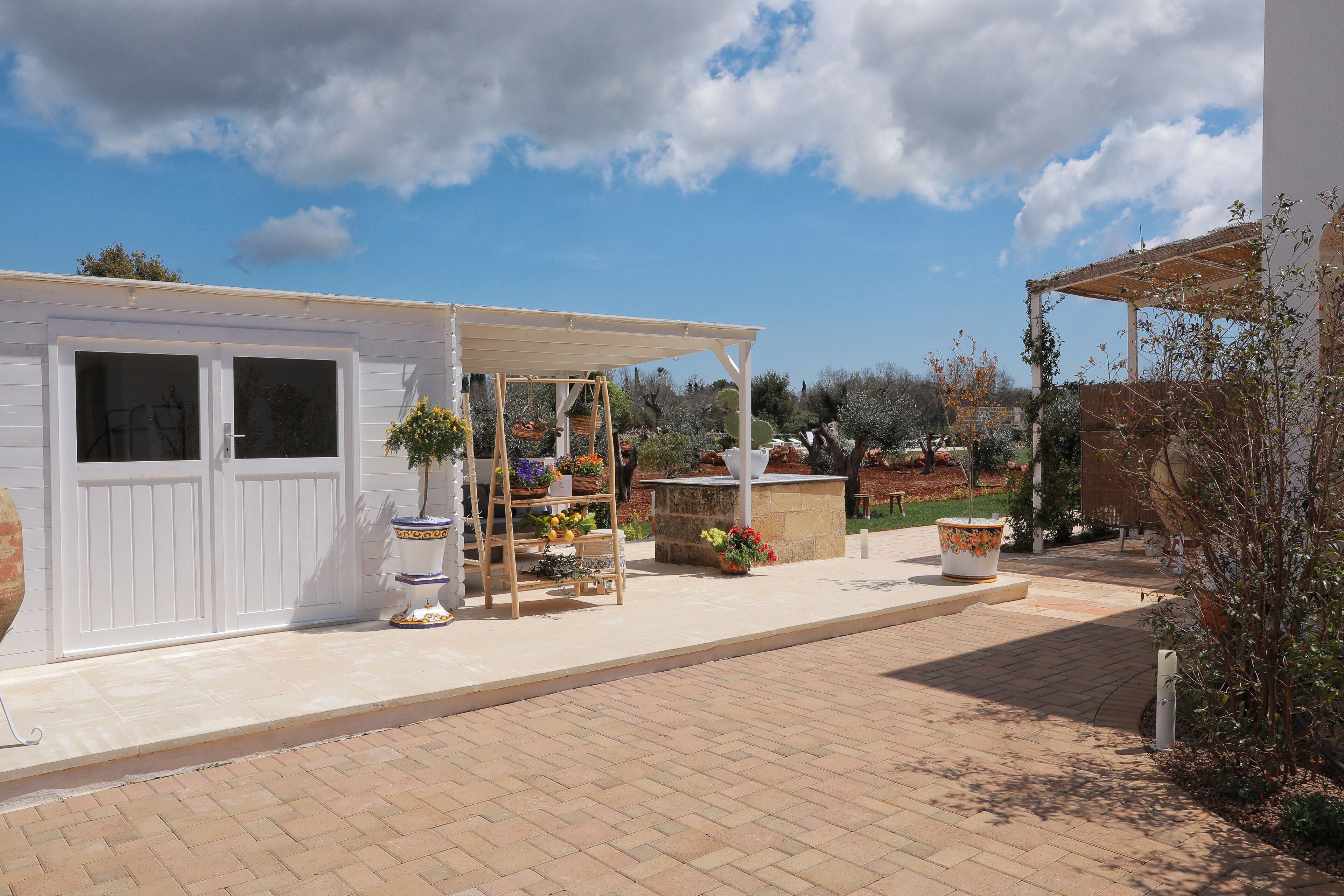 Un patio con una pérgola, plantas en macetas y un banco de piedra.